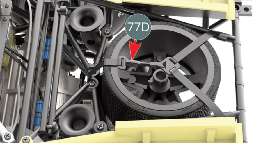 La roue de secours est maintenue par la sangle de la roue de secours 77D située au-dessus.