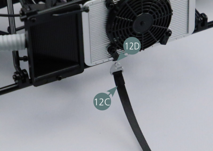 Ligue uma extremidade da correia da roda sobresselente (12C), com o gancho (12D), ao radiador. Passe a correia por trás do radiador.