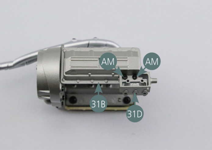 Posiciona la bomba de aceite (31D) en el cárter de aceite (31B). Luego fíjala con dos tornillos AM. Posiciona la tapa de bomba de aceite (31G) en la bomba de aceite (31D) como se muestra en la foto. 