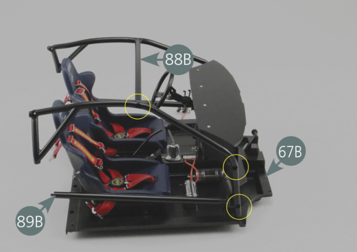 Positionner la cage droite de l’arceau de sécurité 89B sur le plancher droit du cockpit 67B, en prenant soin de faire correspondre les trois trous du montant de l’arceau 89B avec ceux situés sur le panneau du tableau de bord 80A, ainsi qu’avec celui situé à l’extrémité de la barre supérieure de l’arceau 88B (cercles jaunes).