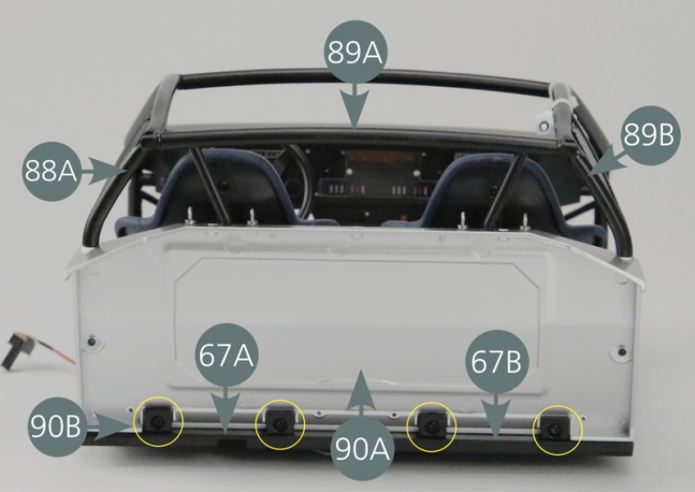 Positionner la cloison arrière 90A en insérant les quatre supports de cloison 90B sur le plancher gauche du cockpit 67A et droit 67B.Insérer les tubes des cages d’arceau de sécurité 88A et 89B dans les trous latéraux (cercles bleus) et ceux du tuyau d’arceau arrière 89A dans les trous supérieurs (cercles rouges) de la cloison. 