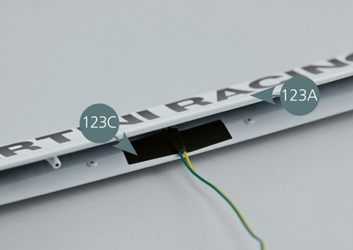 Plier les contacts de la LED à l’aide d’une pince et insérer le câble d’éclairage de la plaque 19B (H1-1) dans le logement prévu sous l’aileron arrière 123A. Fixer le câble avec le ruban adhésif 123C comme indiqué.