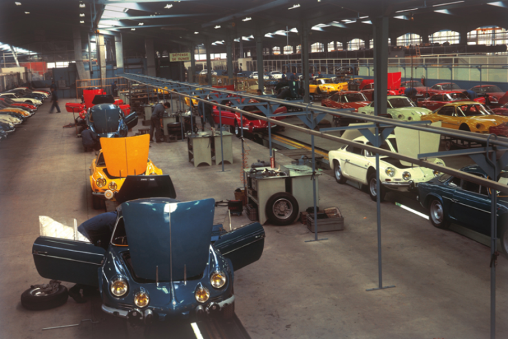 Blick ins Innere der Alpine-Fabrik in Dieppe, 1970. Alpine Berlinettes laufen vom Fließband. Im Vordergrund eine blaue A110, gefolgt von einer gelben, einer weiteren blauen, dann einer roten und schließlich einer weißen A110 rechts. © IXO Collections SAS - Tous droits réservés. Crédits photo ©  Renault D.R.