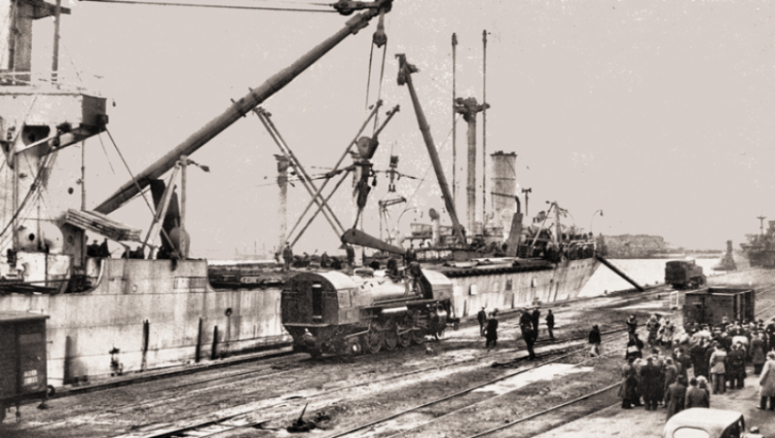 Une rare vue du déchargement d’une 141-R à Cherbourg, en 1946, avec les « mâts de charge » du navire « Belpareil » qui assument la centaine de tonnes de la locomotive. On remarque que la cabine est dépourvue de sa « prolonge » de toiture et fermée par une épaisse plaque de contreplaqué.  © IXO Collections SAS - Tous droits réservés. Crédits photo © Collection Trainsconsultant-Lamming