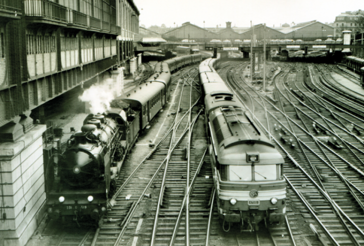 Les « Trente Glorieuses », c’est surtout l’apparition de la traction diesel qui simplifie l’entretien et supprime la traction vapeur. Ici une locomotive Pacific Etat face à sa concurrence incarnée par une diesel type BB-67000 dans la tranchée des Batignolles. Au fond : la gare Saint-Lazare. © IXO Collections SAS - Tous droits réservés. Crédits photo © Collection Trainsconsultant-Lamming